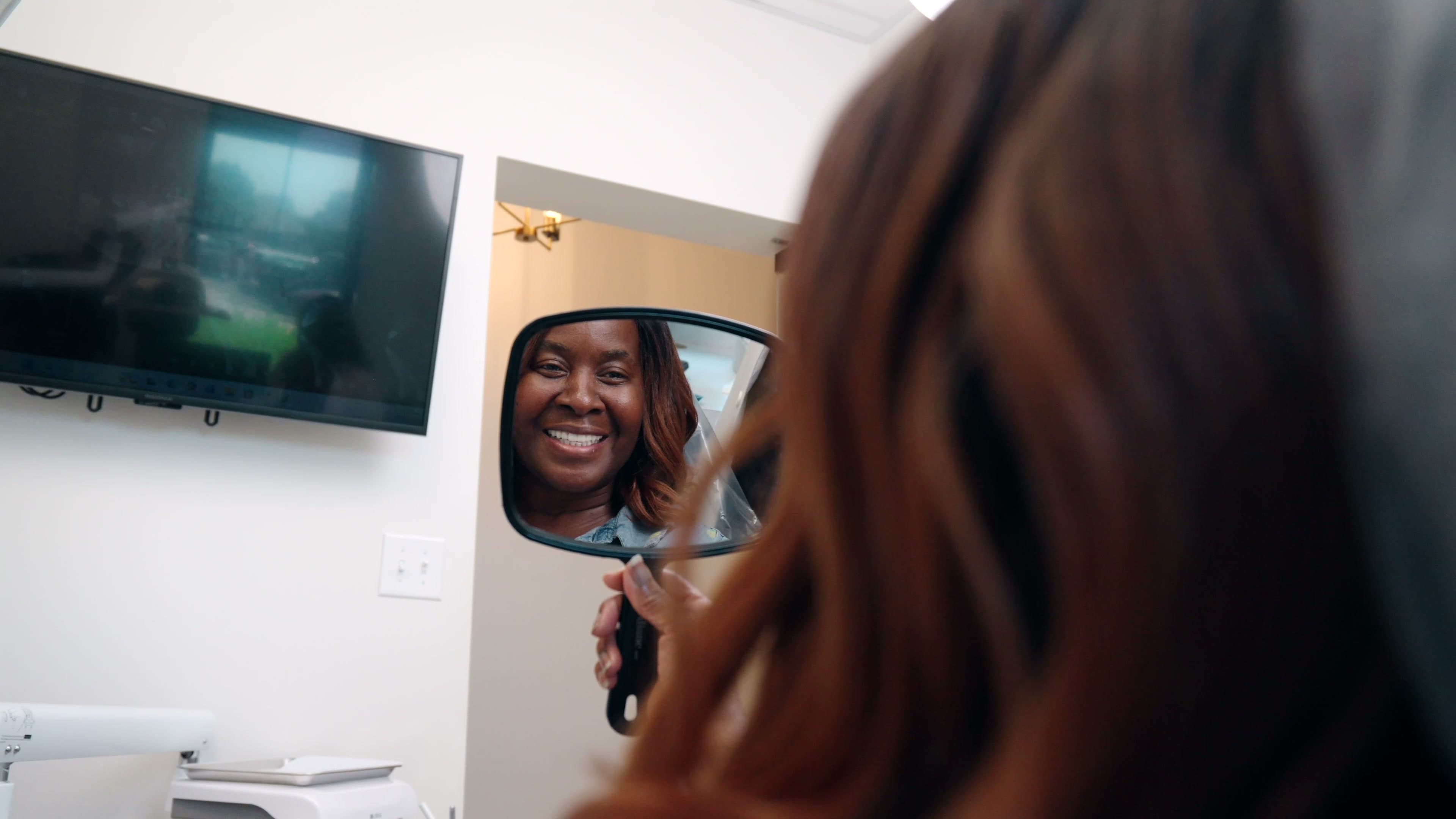 A patient looking at her smile in a hand mirror